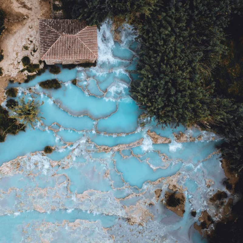 Aerial view of the stunning Maremma hot springs, Tuscany. Turquoise waters, travertine formations, and lush greenery.